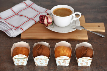 Four mini marble cakes or pound cakes in paper baking moulds in front of white cup of coffee on a wooden board
