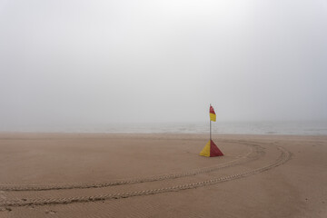 Fototapeta na wymiar The beach of the Baltic Sea in Ventspils, which is covered with a thick fog, but the flag stands on the shore