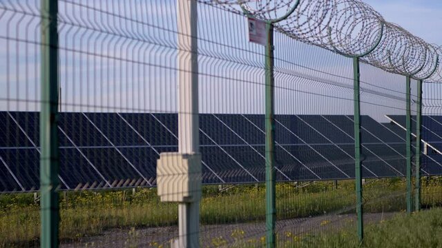 Solar Panels Fenced with Barbed Wire Fence. Solar batteries located on green grass by road, in a protected area behind a wire fence. Electricity generation. Restricted area. Lattice. 4K. Slow motion.