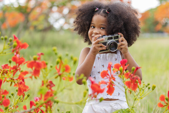 childhood and exploration concept - little african american curly hair girl  taking a photo at red flower garden.