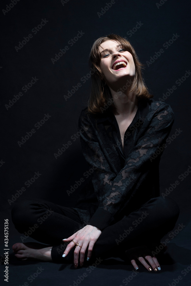 Wall mural young beautiful smiling girl, looking up, closing her eyes, in black, on a black background