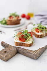 Healthy sandwich with cream cheese, baked tomatoes and micro greens on white background. Healthy breakfast sandwiches on a wooden board