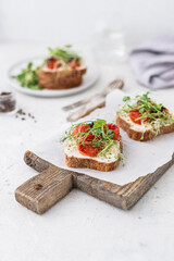Healthy sandwich with cream cheese, baked tomatoes and micro greens on white background. Healthy breakfast sandwiches on a wooden board