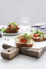 Healthy sandwich with cream cheese, baked tomatoes and micro greens on white background. Healthy breakfast sandwiches on a wooden board