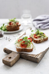 Healthy sandwich with cream cheese, baked tomatoes and micro greens on white background. Healthy breakfast sandwiches on a wooden board