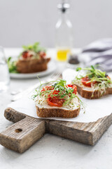 Healthy sandwich with cream cheese, baked tomatoes and micro greens on white background. Healthy breakfast sandwiches on a wooden board