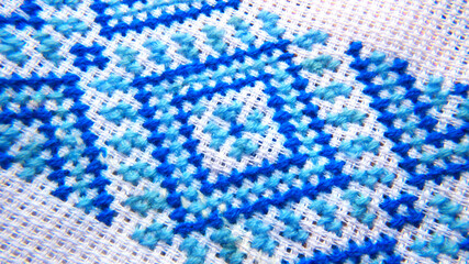 Cross-stitching with blue and light blue threads on white fabric.
