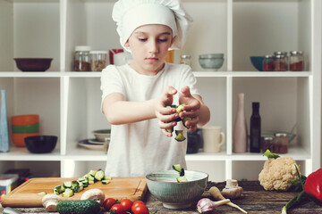 Chef preparing fresh vegan salad in the kitchen. Cute child wearing chef hat cooking healthy vegan...