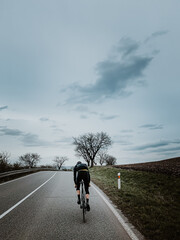 Cyclist riding along a road in autumn. Road cycling in cloudy autumn.