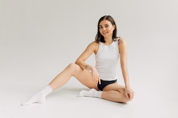 smiling young woman in white top, socks and black panties sitting on grey background
