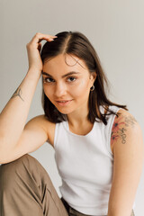 smiling young woman sitting with hand near face and looking at camera on gray background