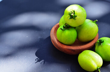 Fresh green cherry tomatoes (Solanum lycopersicum var. cerasiforme) on a wooden bowl, are commonly used in cooking as a garnish and have various health benefits. top view with selective focus