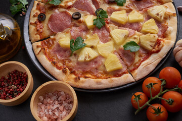 Italian pizza and pizza cooking ingredients on black concrete background. Tomatoes on vine, mozzarella, black olives, herbs and spices. Mixture pizza Italian food. Copy Space. Top view.