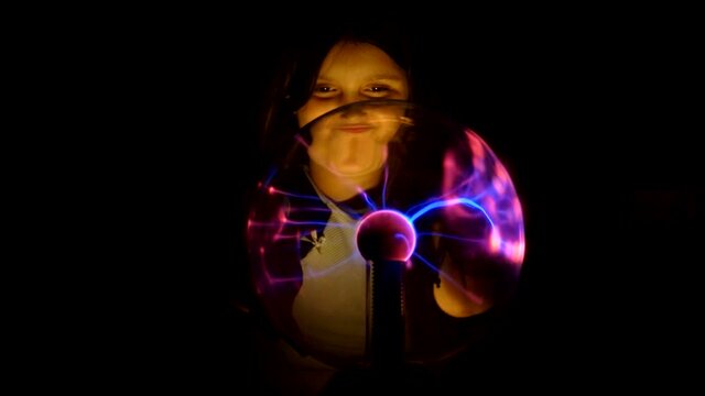 Cute girl moves her fingers across the surface of the plasma Tesla ball