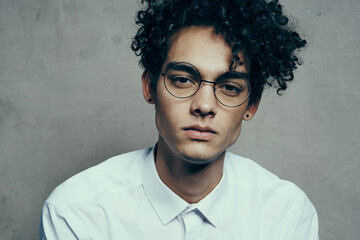 portrait of a nice guy with curly hair on a gray background and a light shirt glasses model close-up