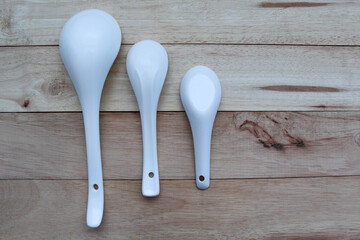 White spoons many size kitchenware isolated on wooden background closeup.