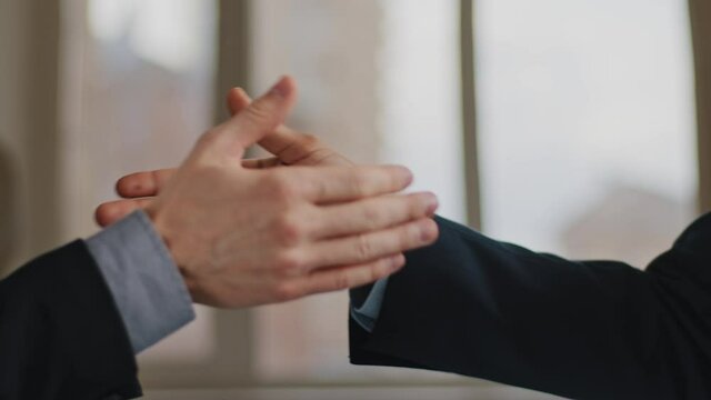 Close-up funny male greeting gesture of partnership, two man African and Caucasian business colleagues clap palms bumping fists waving fingers unusually shaking hands in office near window background