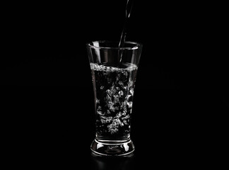 Pouring water into the glass on a black background.