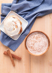 Cinnamon roll, cinnamon sticks, and cinnamon yogurt on wooden surface