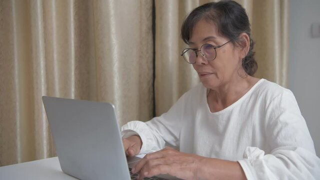 Business concept of 4k Resolution. Asian old lady is working using a computer in the house.