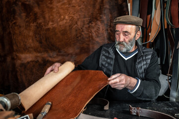 Senior bearded unrolling a leather roll to make in his workshop.