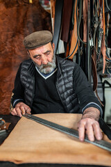 Fototapeta na wymiar Vertical portrait of senior bearded craftsman measuring and working with leather background.