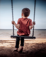 Little boy swinging on the beach looking at the sea into horizon. 