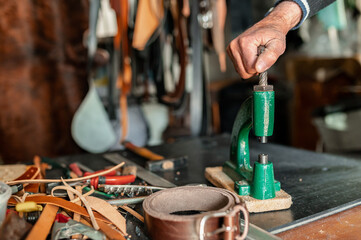 Unrecognizable man hand using a puncher working with leather in a workshop with other tools.