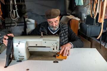 Senior old hipster bearded man with flat cap working with leather ans sewing machine