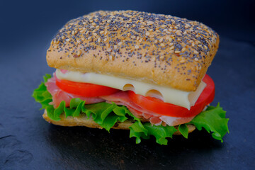 close-up of appetizing sandwich with ripe tomato slices, green lettuce, cheese, ham, ruddy poppy seed bun, quick snack concept, making of fastfood at home, chef is cooking sandwich, fast food, diet