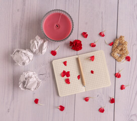 Flat lay with note on white wooden background with pencil, petals and flower and candle and earrings, pieces of paper, candle