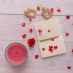 Flat lay with note on white wooden background with pencil, petals and flower and candle and earrings