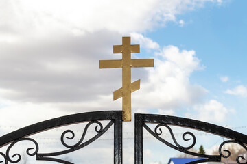 The cross is religious at the gates of the Orthodox Church. Outdoors, front view aganist clouds sky.