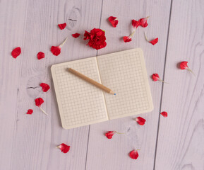 Flat lay with note on white wooden background with pencil, petals and flower