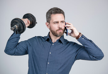 Naklejka premium strong bearded man businessman training with barbell and speaking on smartphone, hello
