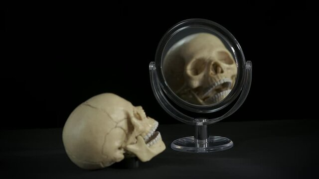 Spooky by mirror. Ungly skull look into a round mirror in the dark.