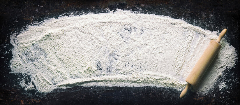 Abstract baking background with the rolling pin and flour on dark table