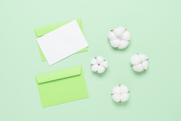 Blank white card mockup and cotton flowers on a green pastel background. Delicate stationery template. Top view, flat lay.
