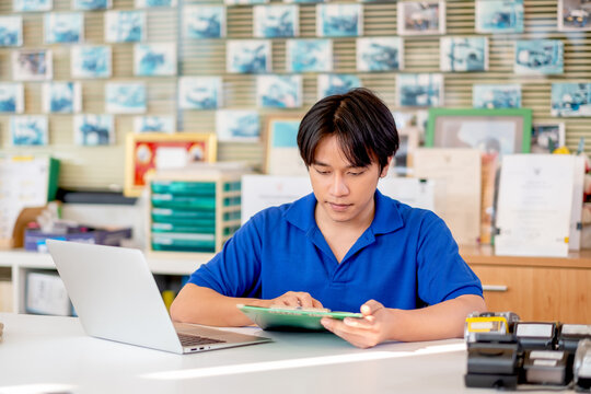 Automotive Or Garage Worker With Blue Shirt Uniform Check List Of Document In The Area Of Counter Service And Use Laptop To Support His Work.