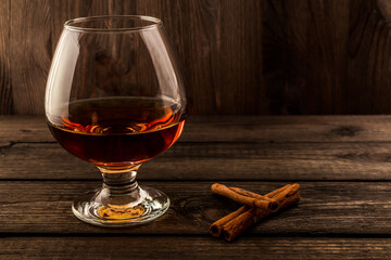 Glass of brandy with cinnamon sticks on a wooden table. Focus on the cinnamon sticks