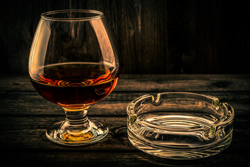 Glass of brandy and glass ashtray on a old wooden table