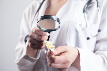 the doctor looks at the pills with a magnifying glass. drug search concept