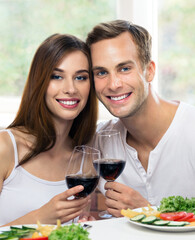 Smiling amorous couple drinking red wine, at home. Caucasian models with redwine glasses in love concept. Happy man and woman posing together indoors.