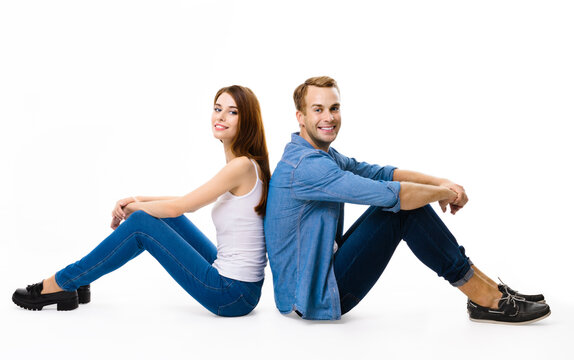 Smiling attractive young couple. Full body profile portrait image of sitting back to back models in love studio concept, isolated over white background. Man and woman posing together.