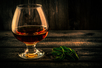 Glass of brandy with mint sprig on an old wooden table. Focus on the mint sprig