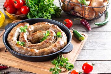 Spiral yummy grilled sausages in pan with vegetable on a table, copy space.