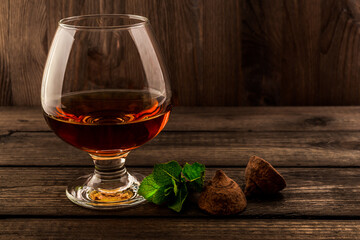 Glass of brandy and a chocolate truffles with mint sprig on an old wooden table. Angle view