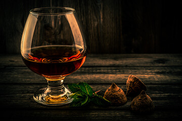 Glass of brandy and a chocolate truffles with mint sprig on an old wooden table. Focus on the...