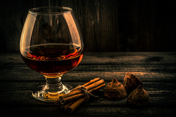 Glass of brandy and a couple of chocolate truffles with cinnamon sticks tied with jute rope on an...