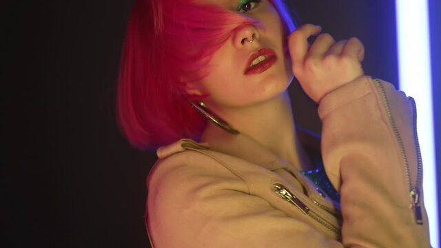 Portrait of party girl dancing to the music on glowing multi-colored lamps in night club. Disco woman with dyed pink hairstyle, glittering hipster outfit. Amazing style.
